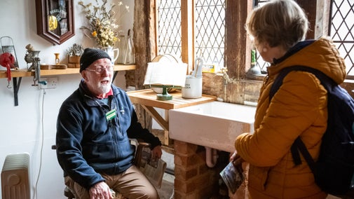 Volunteer sat inside a medieval manor house at Brockhampton, Herefordshire, talking to a visitor